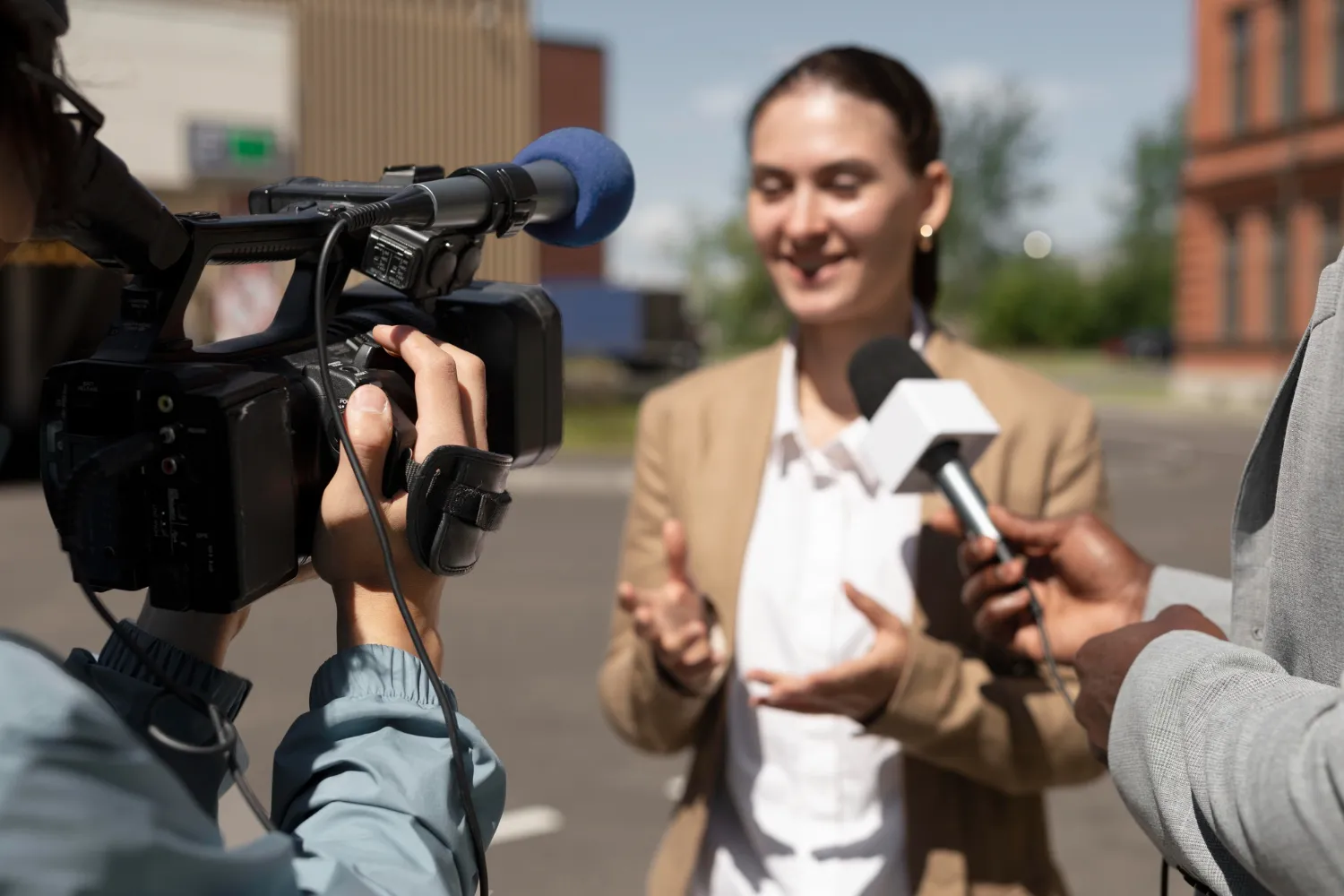 Mujer dando una entrevista al aire libre, mientras un camarógrafo graba con una cámara profesional. Se observan micrófonos y un fondo urbano.